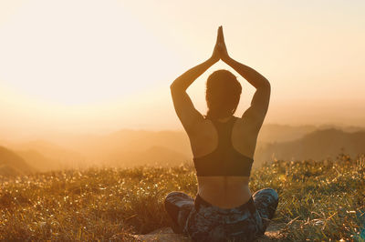 Rear view of woman with arms raised against sky during sunset