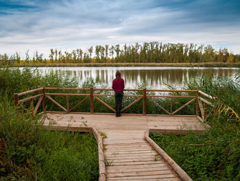 Rear view of man sitting on pier over lake against sky