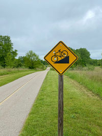 Information sign on road amidst field against sky