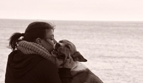 Woman kissing dog at beach against sky