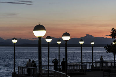 Illuminated lamps on the seattle waterfront after sunset with silhouetted people on a pier 