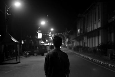 Rear view of man standing on illuminated street at night