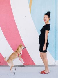 Portrait of young woman with dog standing against wall