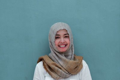 Portrait of smiling mid adult woman wearing hijab standing against wall