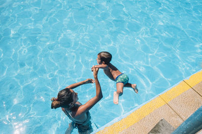 Woman helping child jumping into a pool