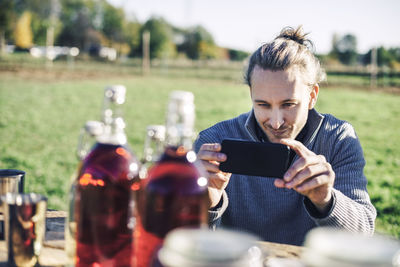 Mid adult man photographing bottles displayed for sale at farmer's market