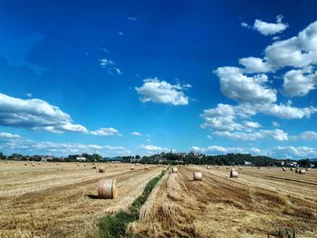 Hay bales on field against blue sky