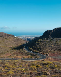 Scenic view of road by sea against clear blue sky