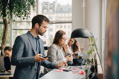 Male professional using laptop and smart phone while working with colleagues at coworking space