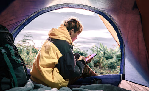 Man using mobile phone while sitting in tent during sunset