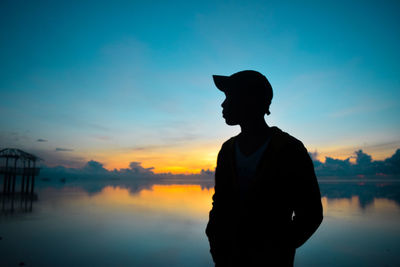 Silhouette man standing by lake against sky during sunset