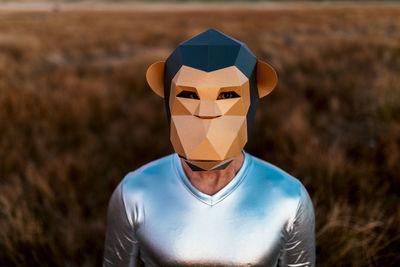 Anonymous person in geometric monkey mask looking at camera in yellow field on blurred background