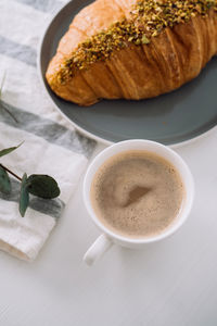 Close up of cup of cappuccino with kitchen towel, croissant and eucalyptus branch on the table	
