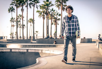 Full length portrait of young man standing against trees in city