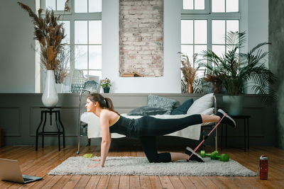 Positive athletic woman with neatly tied hair and tight sportswear doing performs lying kicks 