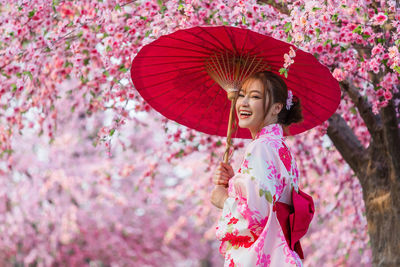 Woman holding umbrella standing by pink flowers