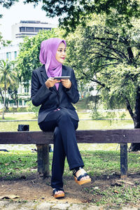 Full length of young woman sitting on bench in park