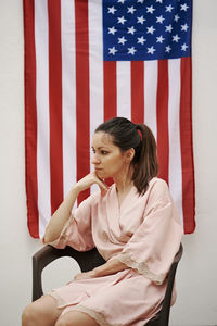 A young girl sitting with the american flag in the background. concept of america