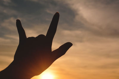 Close-up of silhouette hand gesturing against sky during sunset