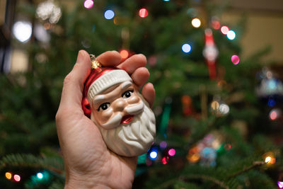 Cropped hand holding santa claus decoration by christmas tree at home