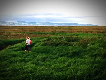 Rear view of woman walking on field against sky