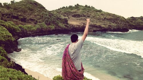 Rear view of man with arm raised standing at beach