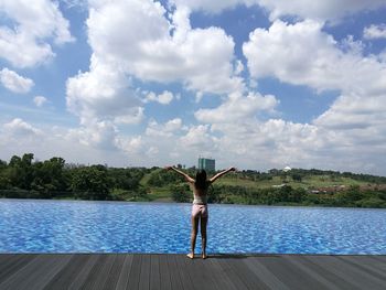 Rear view of woman standing by swimming pool against sky