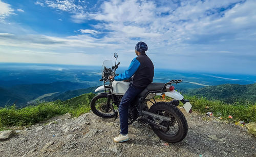 Young man biker sitting on bike at mountain top with mesmerizing view at morning