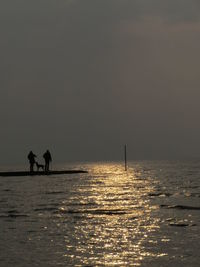 Silhouette people standing on sea against sky during sunset