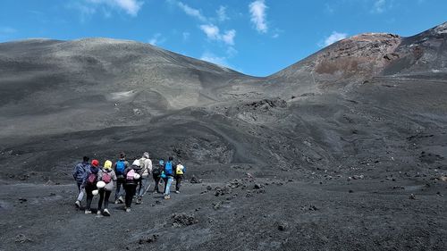 People walking on volcanic crater against sky