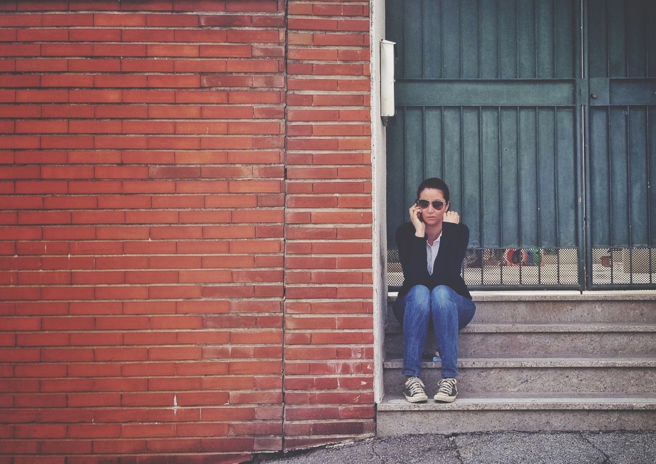 young adult, front view, looking at camera, young women, lifestyles, portrait, building exterior, brick wall, standing, casual clothing, person, built structure, architecture, red, wall - building feature, full length, leisure activity