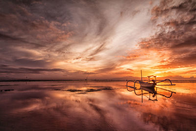 Outrigger boat at beach against cloudy sky during sunset