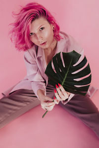 High angle portrait of young woman holding leaf while sitting over colored background