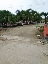 People on footpath by street against sky