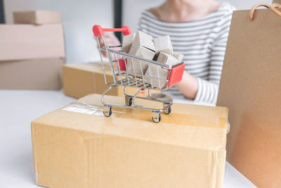 Close-up of miniature shopping cart on cardboard box against woman