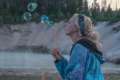 Side view of young woman blowing bubbles at beach