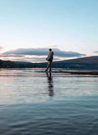Side view of boy standing by lake against sky