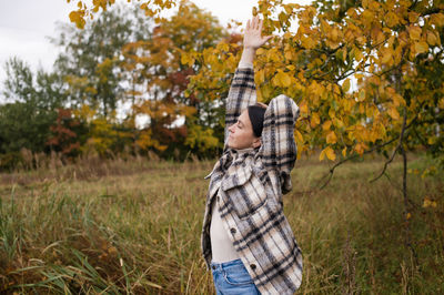 A woman in warm clothes in the autumn forest raised her hands up to stretch and closed her eyes