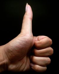 A close-up of human thumb up against black background for your good job and your lovely result