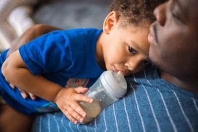 Father at home holding toddler boy while drinks formula from bottle caring and enjoying each other