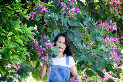 Portrait of beautiful young woman standing by flowering plants