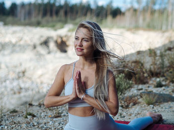 Young beautiful blond woman with long hair in activewear doing leg-split in outdoor training in hill