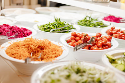 A variety of fresh vegetables and salads are neatly arranged in bowls at a buffet.