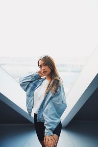 Portrait of young woman standing against window