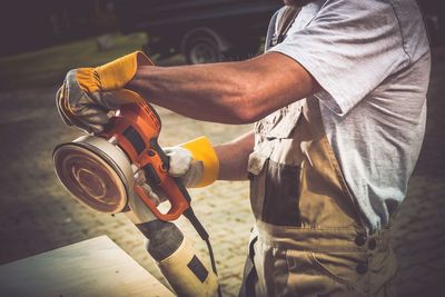 Midsection of carpenter using sander in workshop