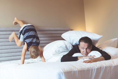 Father lying while son playing on bed at home