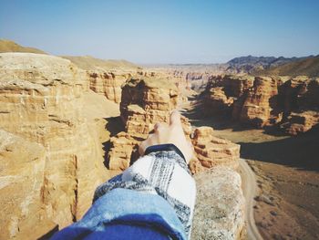 Cropped hand pointing at rock formations against sky