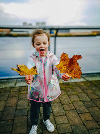 Full length of girl holding autumn leaves standing outdoors