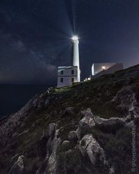 Lighthouse by sea against sky at night