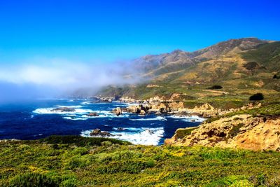 Scenic view of sea and mountains against blue sky